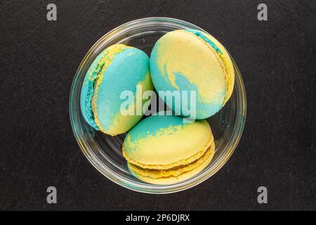 Trois produits de confiserie, macarons doux dans une assiette de verre sur pierre d'ardoise, macro, vue du dessus. Banque D'Images