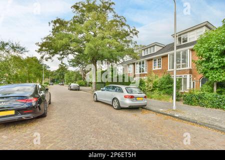 Amsterdam, pays-Bas - 10 avril 2021 : deux voitures garées dans la rue en face d'un immeuble d'appartements, avec des arbres et des buissons qui poussent le long de la route Banque D'Images