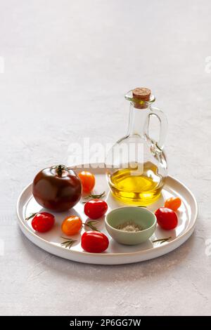 plateau rond avec différentes variétés de tomates, servi avec du sel et de l'huile d'olive, vue latérale, espace copie Banque D'Images