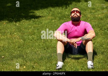 Portrait d'un cycliste professionnel en vêtements de sport, se repose et profite du soleil dans le parc, copyspace. Le concept d'un actif et sain Banque D'Images