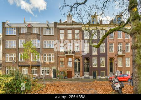 un immeuble d'appartements dans les feuilles d'automne sont éparpillés sur le sol, et il y a une voiture rouge garée à côté Banque D'Images