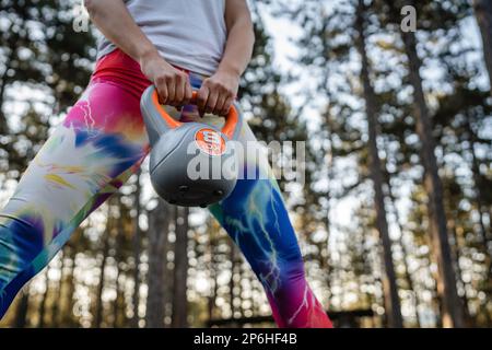 Mi-section d'une femme caucasienne inconnue athlète féminine portant un poids en plastique kettlebell girya en se tenant dans un parc naturel ou une forêt pendant l'entraînement i Banque D'Images