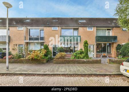 une vue extérieure d'une maison avec des voitures garées dans l'allée et des plantes poussant sur le côté du bâtiment Banque D'Images