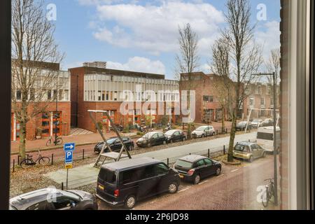 une zone extérieure avec des voitures garées dans la rue et des bâtiments en arrière-plan, prises d'une fenêtre donnant sur Banque D'Images