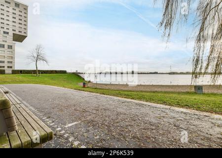 Amsterdam, pays-Bas - 10 avril 2021 : banc sur le côté d'une route à côté d'un plan d'eau avec arbres et bâtiments en arrière-plan Banque D'Images