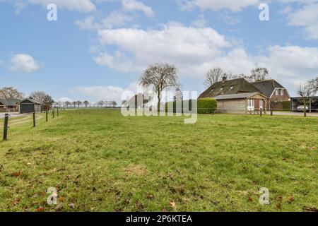 un champ herbacé avec des maisons au loin et des arbres de l'autre côté de la photo, pris d'un angle Banque D'Images