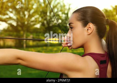 Femme avec arc et flèche pratiquant le tir à l'arc dans le parc Banque D'Images