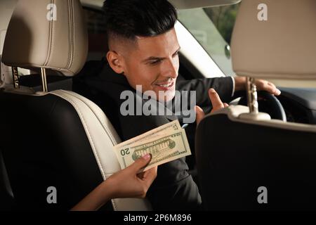 Jeune femme donnant de l'argent chauffeur de taxi dans la voiture moderne, à proximité Banque D'Images