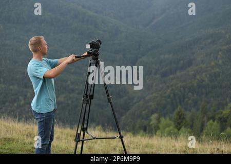 Photographe prenant des vidéos avec un appareil photo moderne sur trépied en montagne Banque D'Images