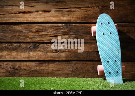 Planche à roulettes bleu clair avec roues roses sur herbe verte près du mur en bois, espace pour le texte Banque D'Images