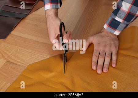 Homme coupant le cuir orange avec des ciseaux à la table en bois, gros plan Banque D'Images