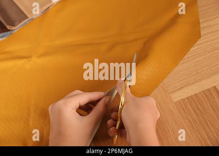 Femme coupant le cuir orange avec des ciseaux à la table en bois, gros plan Banque D'Images