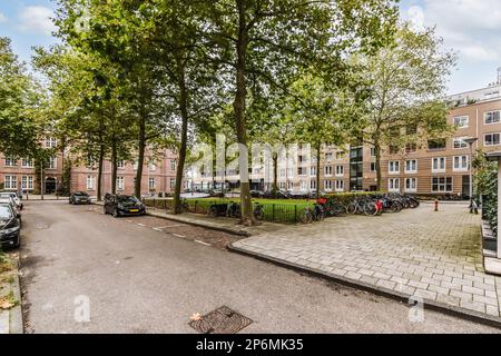 Amsterdam, pays-Bas - 10 avril 2021 : rue de la ville avec des voitures garées et des arbres au milieu de la rue, entourée de bâtiments de chaque côté Banque D'Images