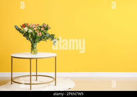 Vase avec de belles fleurs d'alstroemeria sur la table près du mur jaune Banque D'Images
