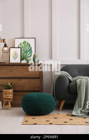 Intérieur élégant du salon avec pouf tricoté, canapé et commode en bois Banque D'Images