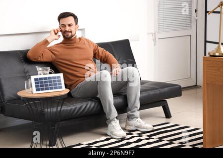 Beau homme parlant par téléphone portable près du panneau solaire portable à la maison Banque D'Images