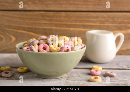 Bol d'anneaux de céréales colorés et pichet avec lait sur table en bois gris Banque D'Images