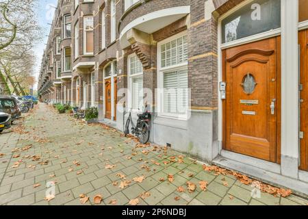 laisse sur le sol devant un immeuble d'appartements avec un vélo garé à côté et deux voitures garées le long du trottoir Banque D'Images