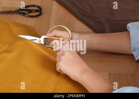 Femme coupant le cuir orange avec des ciseaux à la table en bois, gros plan Banque D'Images