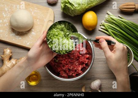 Femme ajoutant le chou haché à gyoza se remplissant à table en bois, vue de dessus Banque D'Images