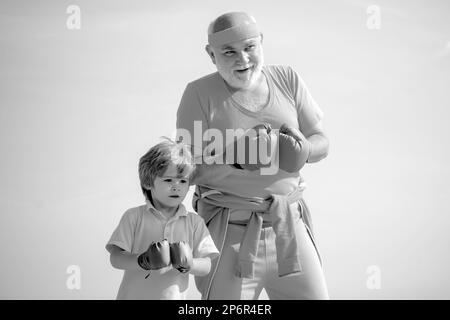 Homme âgé heurtant un sac de poinçonnage. Boxe. J'aime la boxe. Portrait d'un boxeur senior déterminé avec un petit garçon enfant sur fond bleu ciel. Banque D'Images