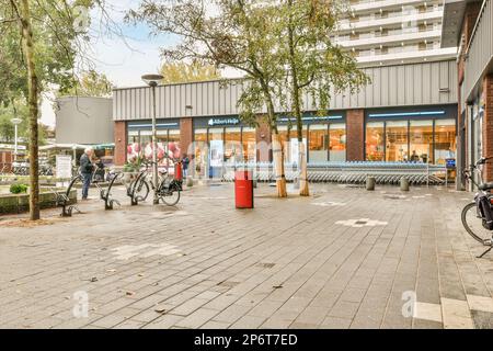 Amsterdam, pays-Bas - 10 avril 2021 : les personnes marchant et faisant du vélo sur le trottoir devant un immeuble de bureaux, avec des arbres bordant le côté de la rue Banque D'Images