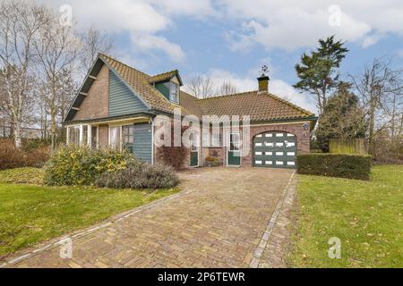 une maison avec une allée à l'avant et deux garages de l'autre côté, entourée d'herbe verte Banque D'Images