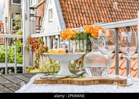 un cadre extérieur avec des fleurs dans des vases et des verres à vin sur une table en bois à côté d'un bol blanc rempli de fruits Banque D'Images