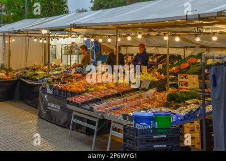 un marché extérieur avec des fruits et des légumes à vendre dans la lumière du soir, sur une rue pavée de briques bordée de gens Banque D'Images