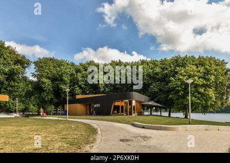 Amsterdam, pays-Bas - 10 avril 2021 : un parc avec quelques arbres et des personnes assises sur le banc en face du lac sous un ciel bleu vif rempli de nuages blancs Banque D'Images