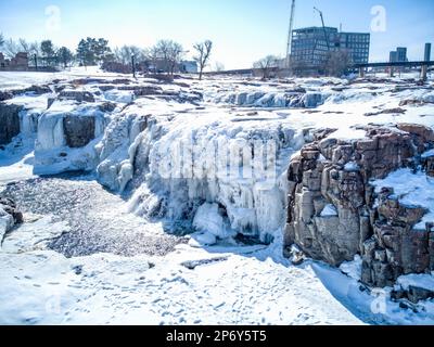 Chutes d'eau du parc Sioux Falls avec glace et neige. Cascade d'eau de fonte de neige qui coule sur le dessus dans une piscine d'eau stagnante. Banque D'Images