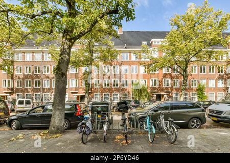 Amsterdam, pays-Bas - 10 avril 2021 : deux vélos garés devant un grand bâtiment en briques avec de nombreuses fenêtres sur le côté et des voitures garées à côté des autres bâtiments Banque D'Images