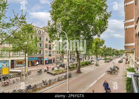 Amsterdam, pays-Bas - 10 avril 2021 : rue de la ville avec des personnes marchant et des vélos garés sur le côté de la route devant quelques grands bâtiments Banque D'Images