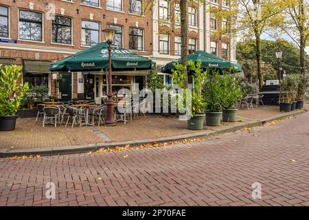 Amsterdam, pays-Bas - 10 avril 2021 : restaurant extérieur avec tables et parasols sur le trottoir devant un bâtiment en briques, entouré d'arbres Banque D'Images