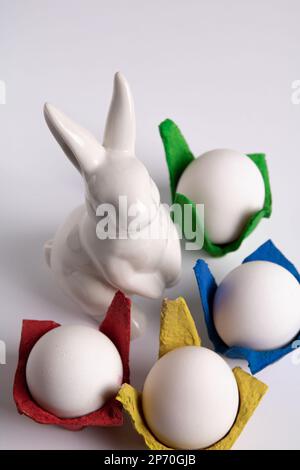 photo des œufs dans des cellules multicolores et un lapin blanc en céramique sur fond blanc Banque D'Images