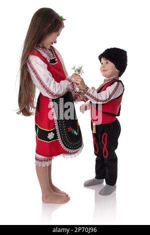 Garçons et filles bulgares en costumes traditionnels folkloriques avec fleurs printanières en forme de goutte d'eau et bracelet en laine martenitsa, symbole de Baba Marta Banque D'Images