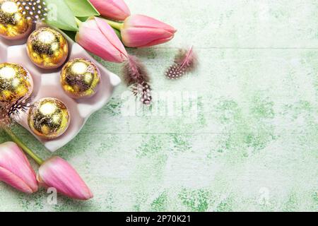 Porte-œufs de Pâques peint de couleurs dorées et tulipes roses sur fond de bois vert. Vue de dessus. Espace pour le texte. Banque D'Images