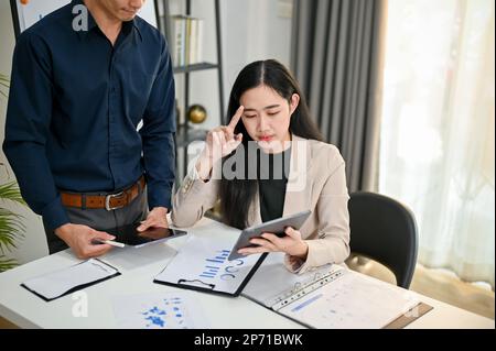 Une femme d'affaires asiatique sérieuse et réfléchie du millénaire ou une analyste financière féminine est dans la réunion avec son collègue, analysant la da financière d'affaires Banque D'Images