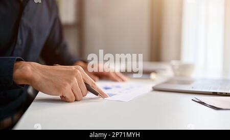 Image rognée d'un homme d'affaires asiatique ou d'un travailleur financier du millénaire qui passe en revue le rapport de données financières de l'entreprise à son bureau Banque D'Images