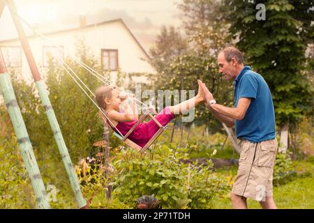 Jolie petite fille sur une balançoire. Enfant souriant jouant avec Grandpa en plein air en été Banque D'Images