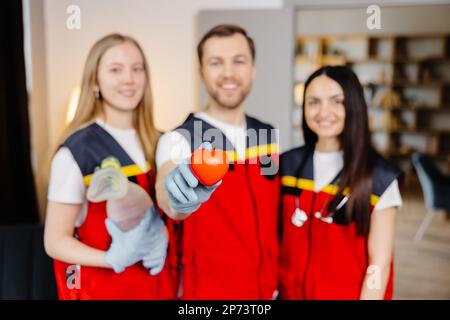 Un groupe de jeunes médecins en uniforme se tiennent au milieu de la classe et sourit après une leçon de premiers soins. Un homme tient un cœur rouge dans son han Banque D'Images