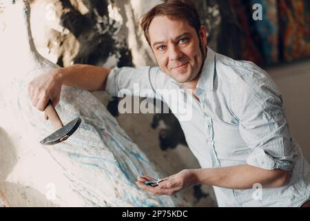 Le portrait de maître de l'artisan tient un marteau et des morceaux de verre de smalt dans la main de bras pour l'art de mosaïque dans l'atelier. Banque D'Images