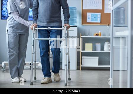 Section basse de l'homme âgé utilisant un marcheur de mobilité en clinique avec l'aide d'une infirmière, espace de copie Banque D'Images