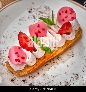 Eclairs à la crème et aux fraises sur une assiette blanche. gros plan sur la table, service dans un restaurant, concept de menu. Banque D'Images