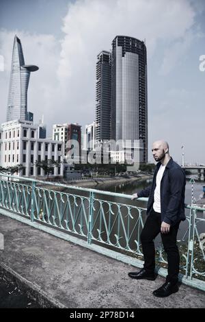 Un homme à tête chauve habillé à la fois décontracté et debout sur un pont contre le paysage urbain. Jeune homme caucasien confiant dans une rue de ville Banque D'Images