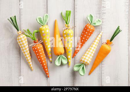 Des carottes en peluche avec des oreilles de lapin sur des planches de bois blanches. Concept de vacances de Pâques. Banque D'Images