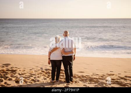 Couple âgé se embrassant sur la plage vue de leur dos Banque D'Images