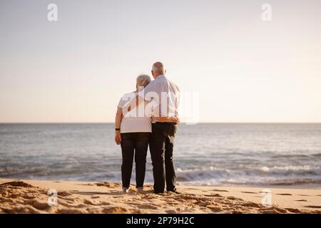Couple âgé se embrassant sur la plage vue de leur dos Banque D'Images