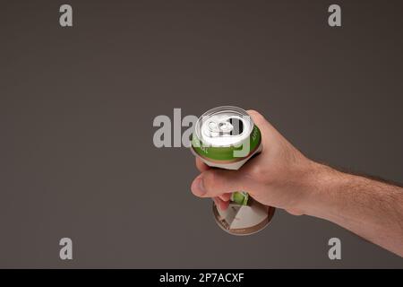 Mâle caucasien tenant une boîte de bière en étain-métal concassée. Gros plan en studio, isolé sur fond marron. Banque D'Images