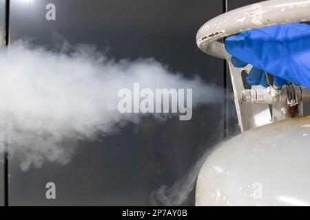 Main de l'opérateur dans un gant de protection bleu libérant la vanne de pression d'un réservoir d'azote liquide. Gros plan... Banque D'Images